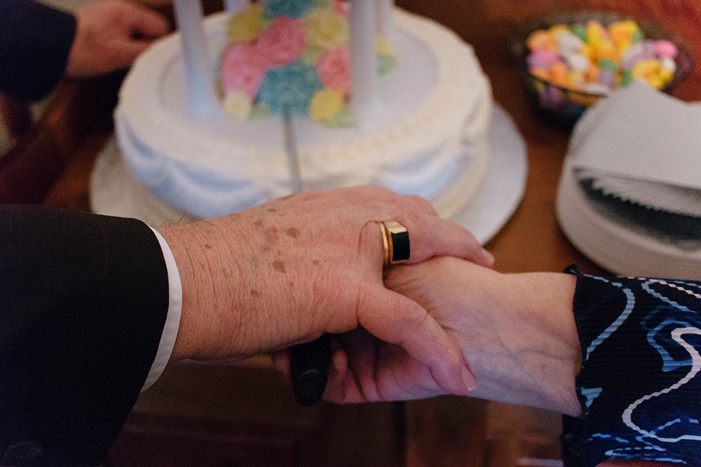 A couple holding hands in front of a wedding anniversary cake